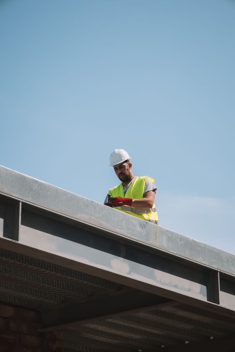 A worker in safety gear standing on a rooftop against a clear sky in Málaga, Spain.