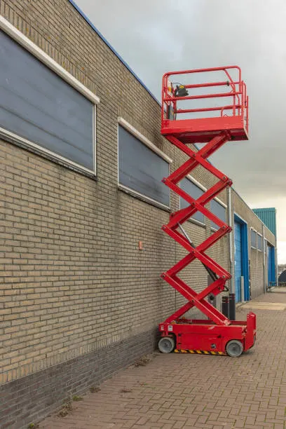 red-scissor-lift-is-parked-outside-a-factory-facade